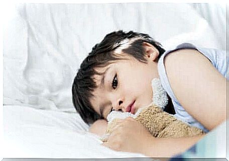 A young boy lying with a teddy bear in his arms. 